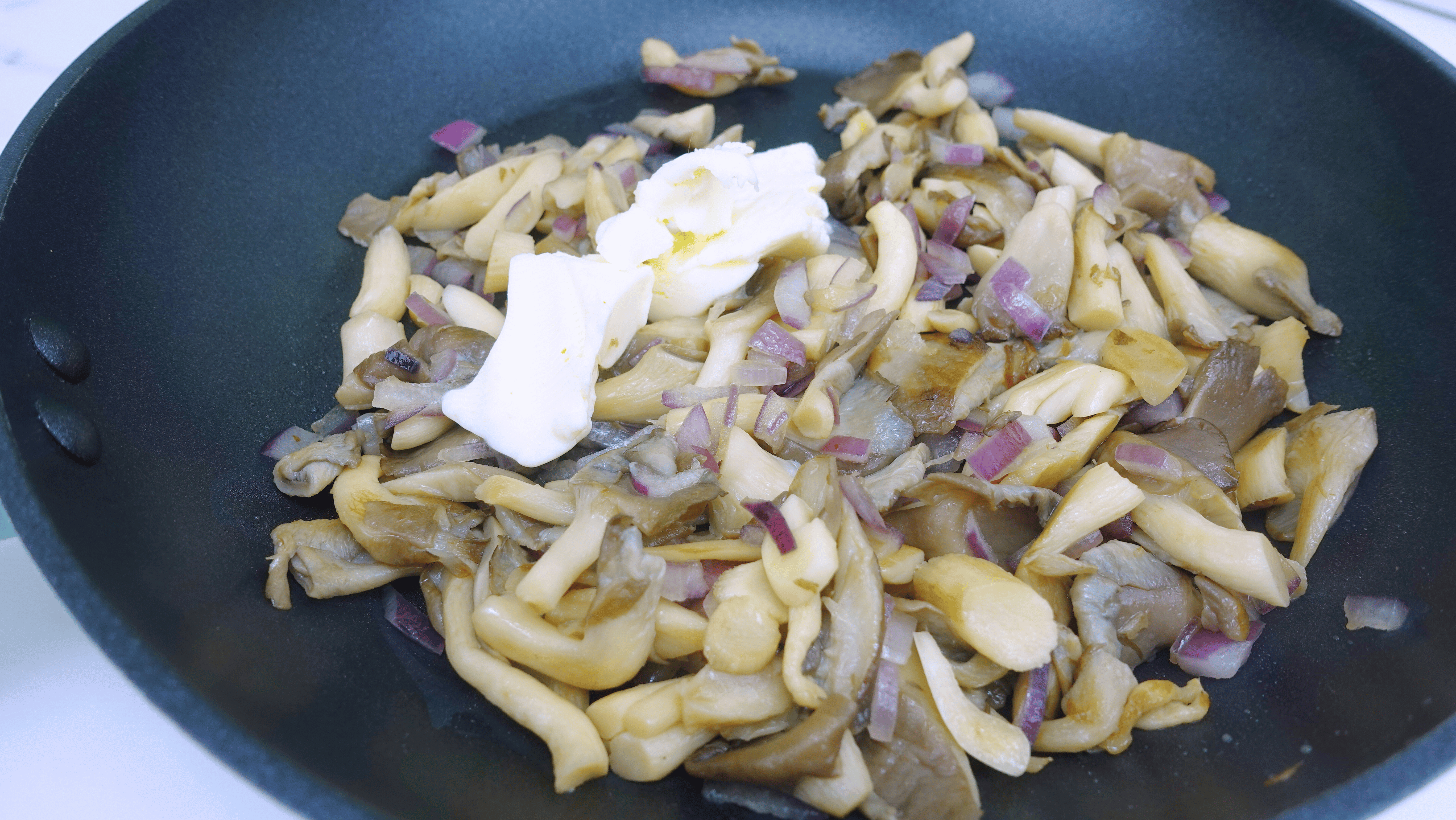 Adding butter to mushrooms frying in a skillet.