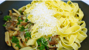 Adding Parmesan cheese to mushroom pasta in a skillet.