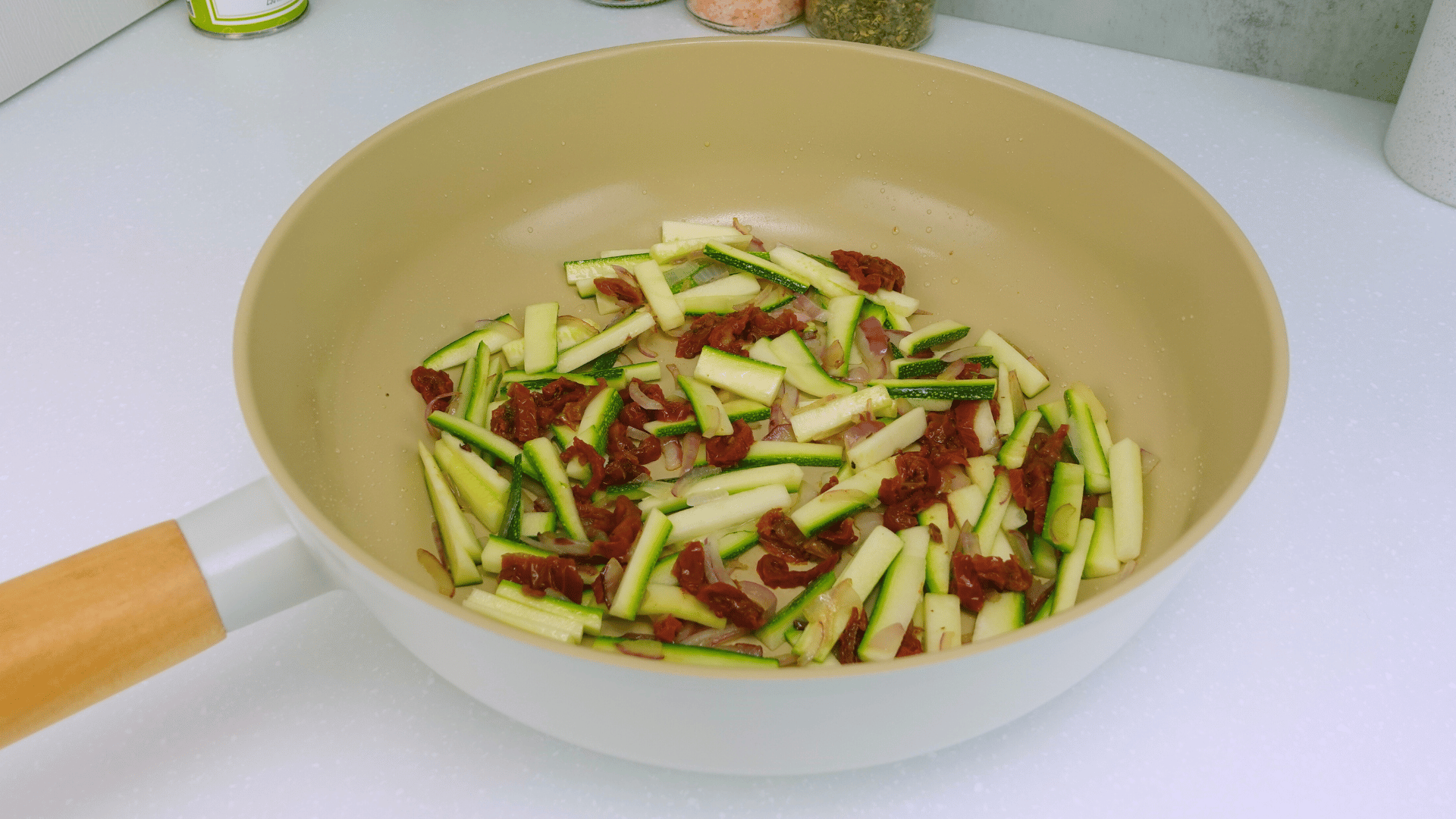 Adding zucchini and sun-dried tomatoes to the pan and sautéing until tender.