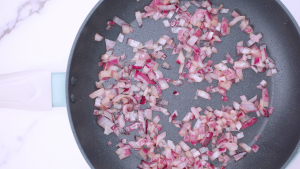 Ground beef sizzling in a skillet with chopped onion and garlic in olive oil.