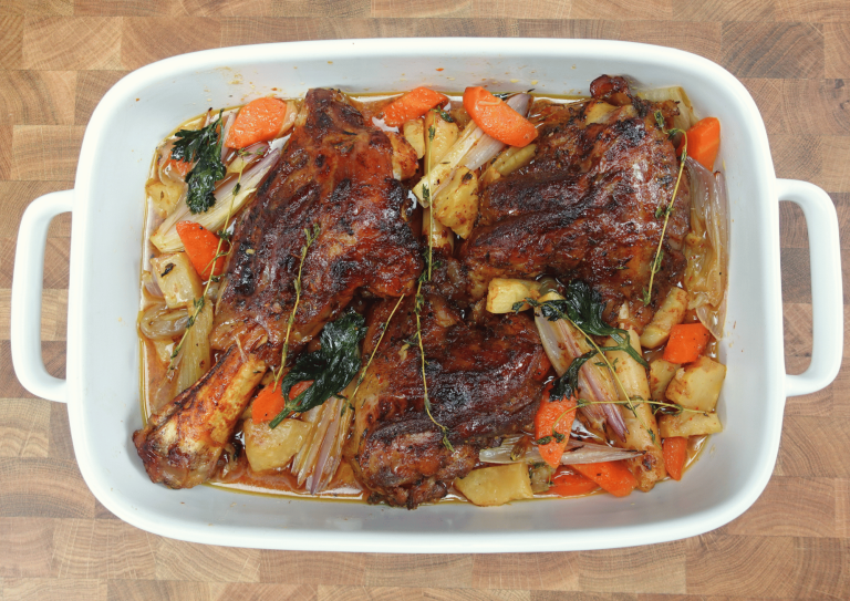 Slow-cooked lamb shank on a rustic plate with tender, juicy meat, surrounded by a rich, savory sauce. Garnished with fresh herbs and served with roasted vegetables for a hearty meal.