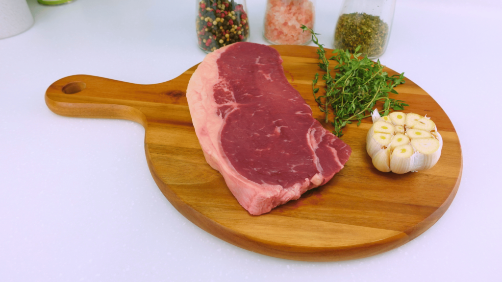 Porterhouse steak with garlic and thyme on a wooden board.