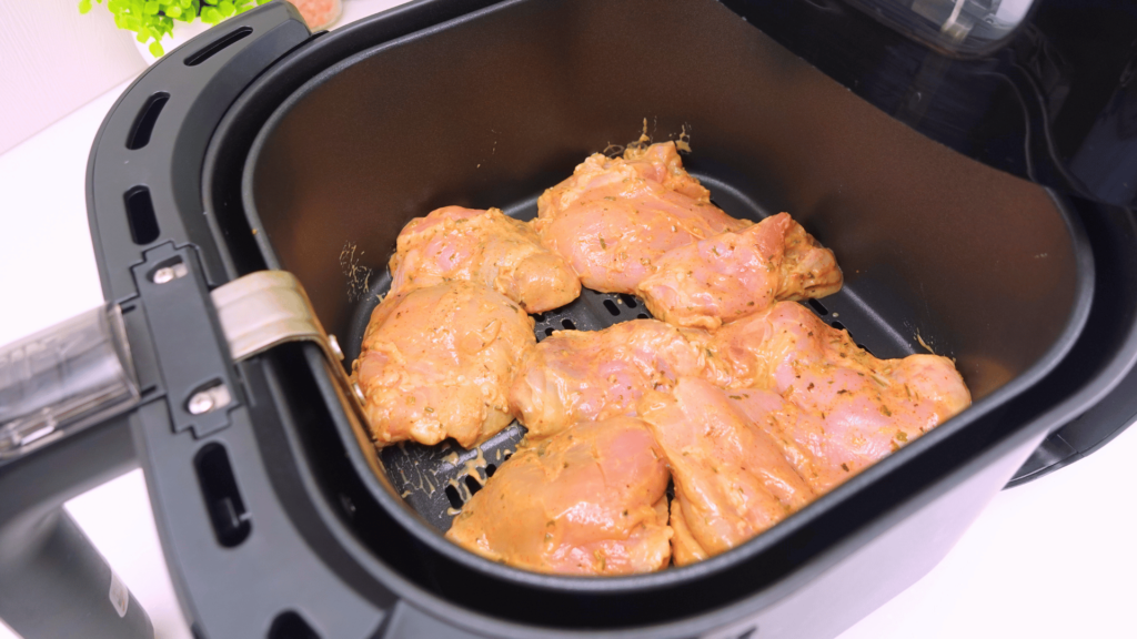 Raw marinated chicken thighs placed in an air fryer.