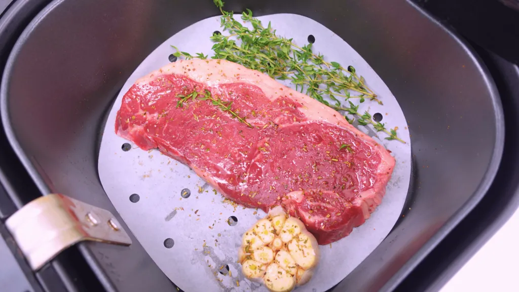 Close-up top view of steak with garlic and thyme in an air fryer.