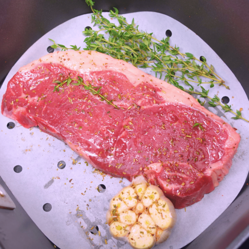 Close-up top view of steak with garlic and thyme in an air fryer.