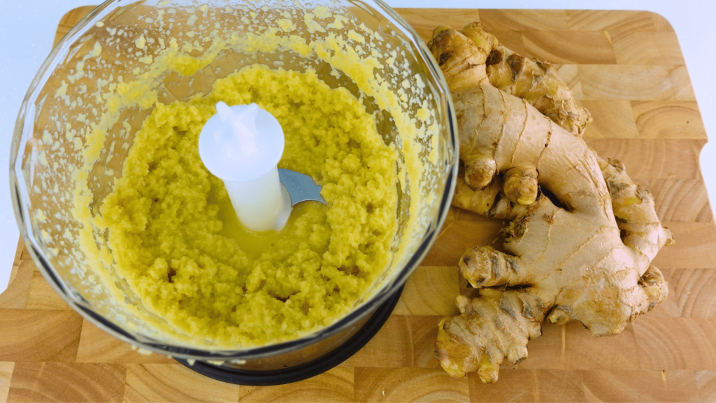 Blended ginger pulp in a blender bowl next to whole unpeeled ginger.