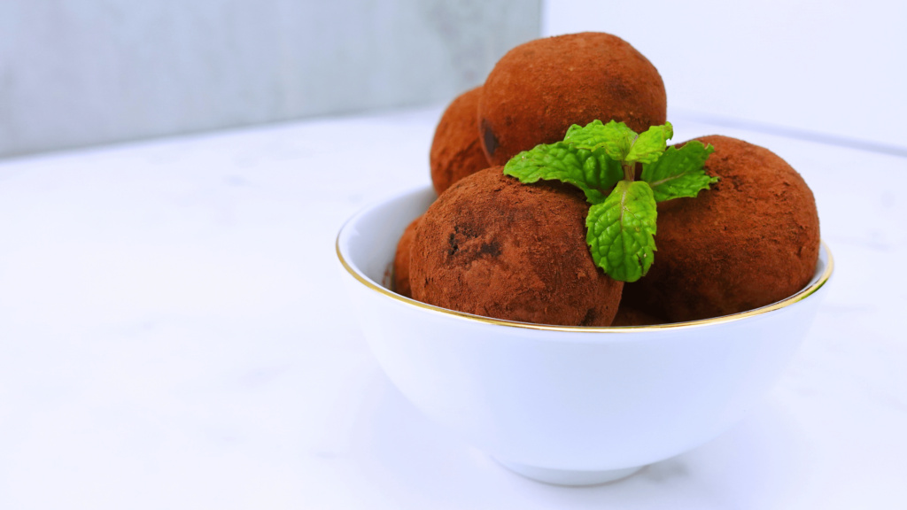 Beautiful presentation of cacao nibs truffles in a small bowl on a white background with fresh mint leaves.