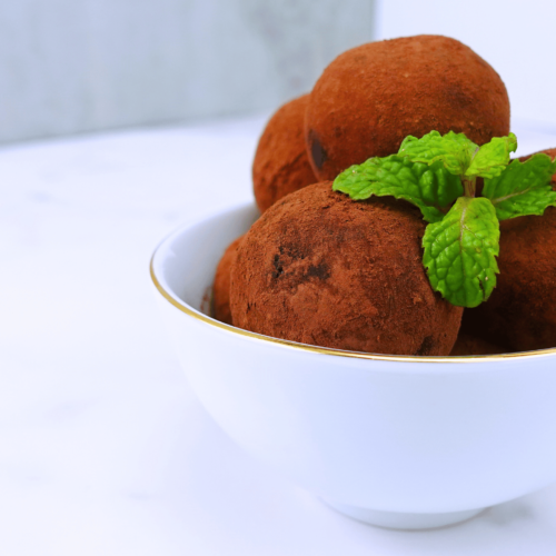 Beautiful presentation of cacao nibs truffles in a small bowl on a white background with fresh mint leaves.