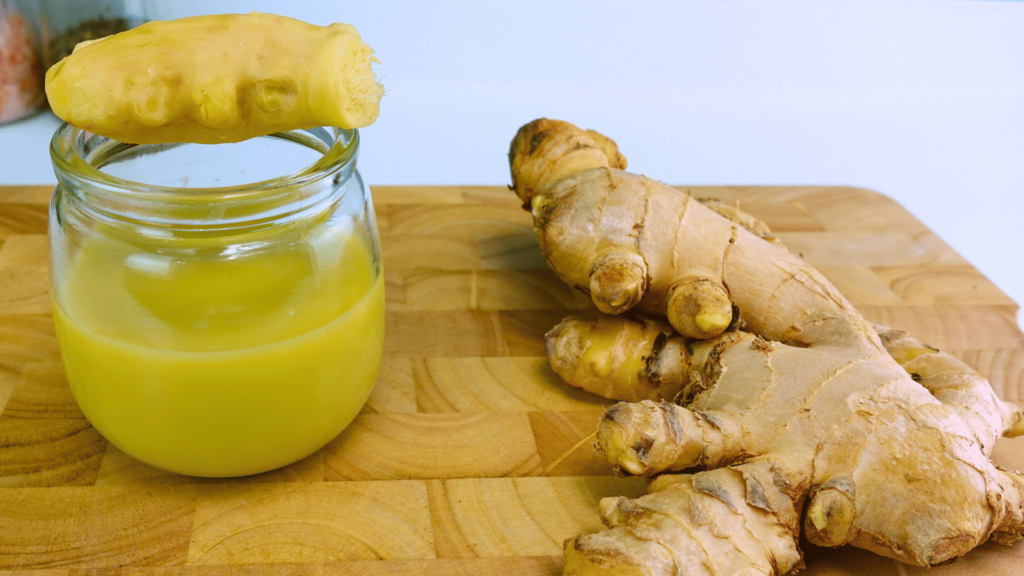 Juice of Ginger in a jar placed on a cutting board with peeled ginger resting on the jar.