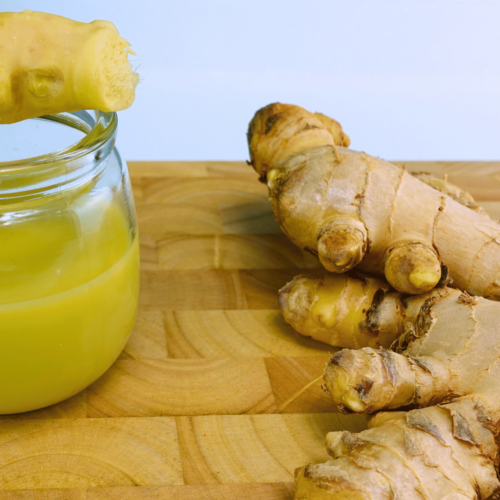 Ginger juice in a jar placed on a cutting board with peeled ginger resting on the jar.