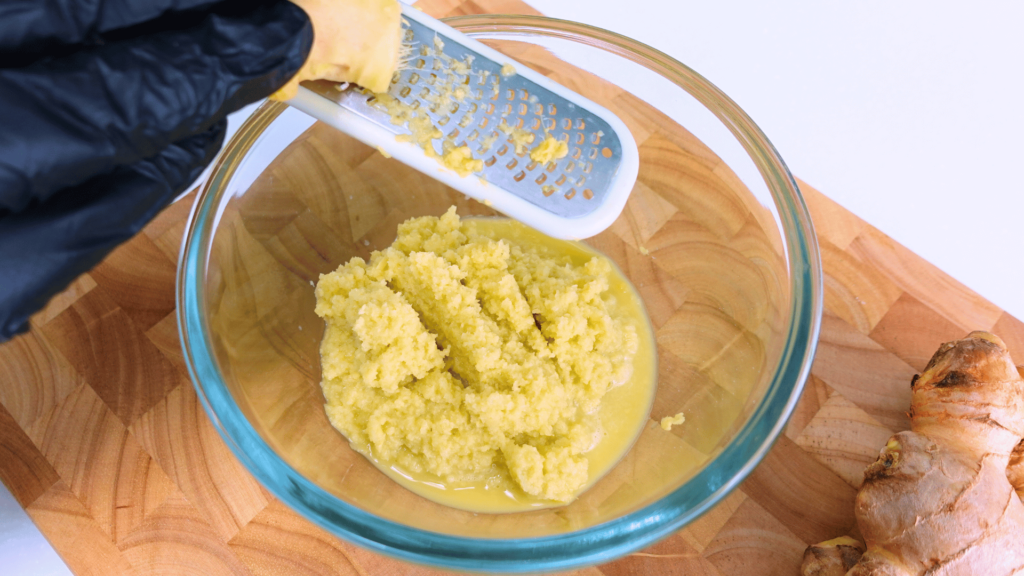 Fresh ginger being grated on a cheese grater, horizontal layout.