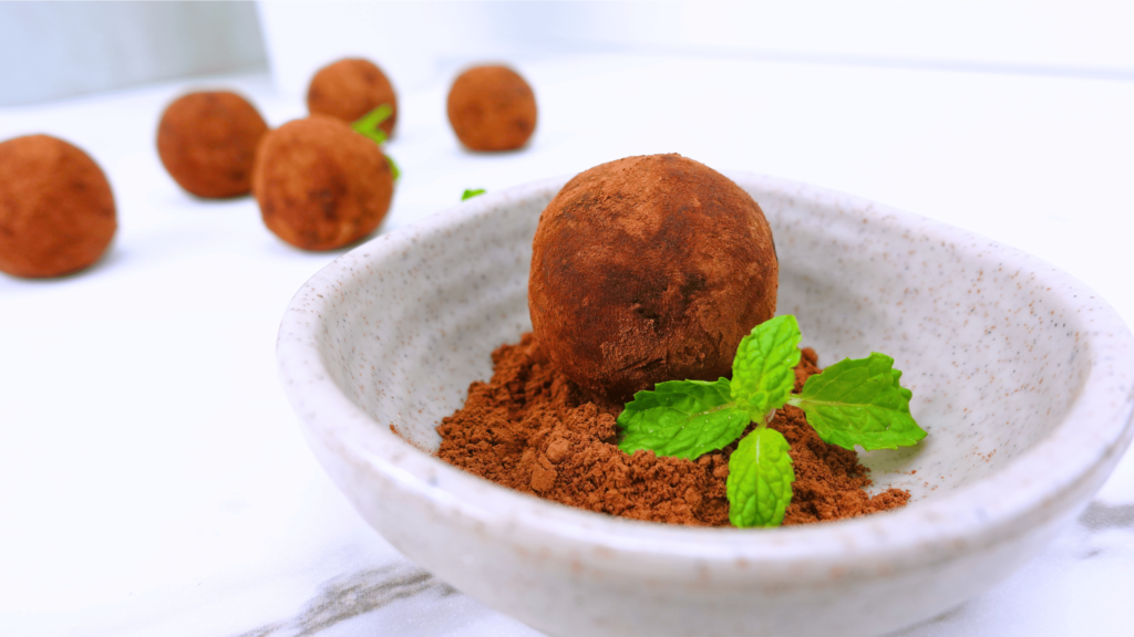 Healthy cacao nibs truffles in a small bowl with cocoa powder and fresh mint.