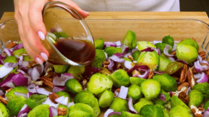 Pouring the prepared sauce over cooked Brussels sprouts and pecans.